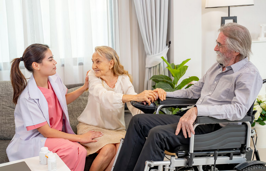 A female home health nurse comforting an elderly woman and her husband in a wheelchair at home.