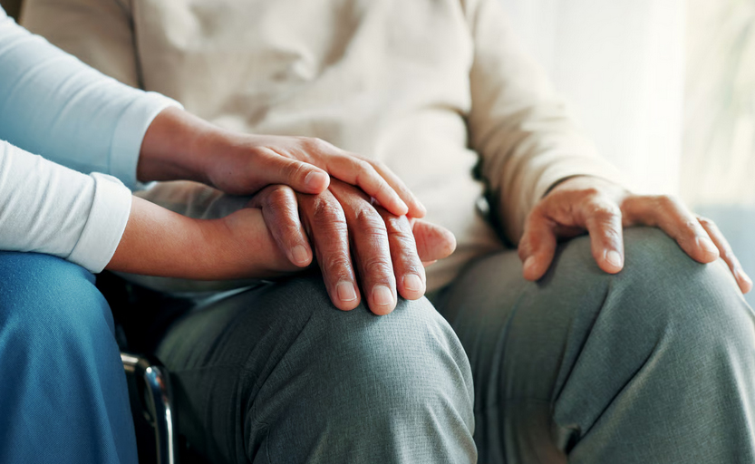 Close-up of a caregiver holding an elderly senior's hand in a supportive gesture at an assisted living facility.