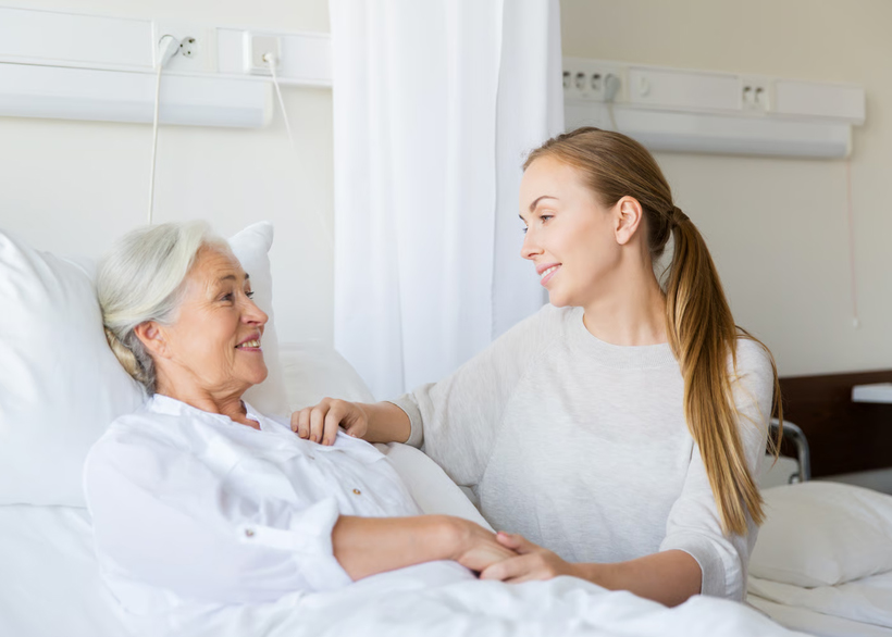 An elderly man receiving comforting support from a young caregiver sitting beside him on a sofa.